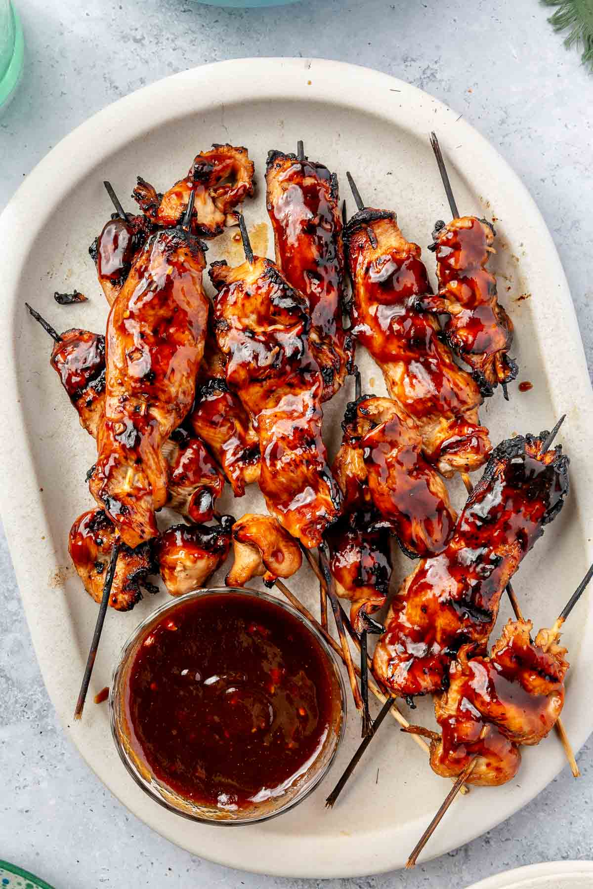 Glazed chicken skewers on a serving plate with BBQ sauce.