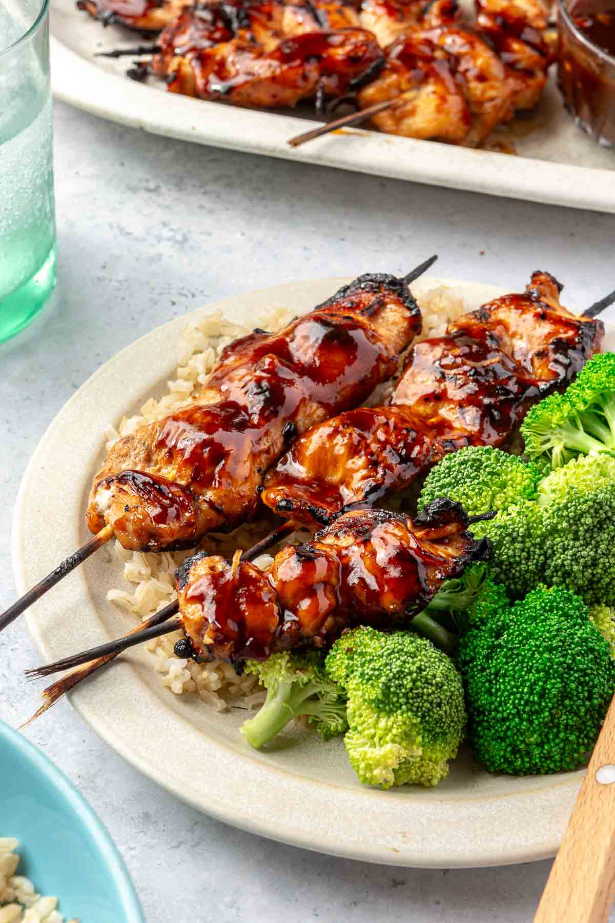 Glazed chicken skewers on a plate with rice and broccoli.