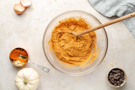 stirring pumpkin cookie batter with a wooden spoon