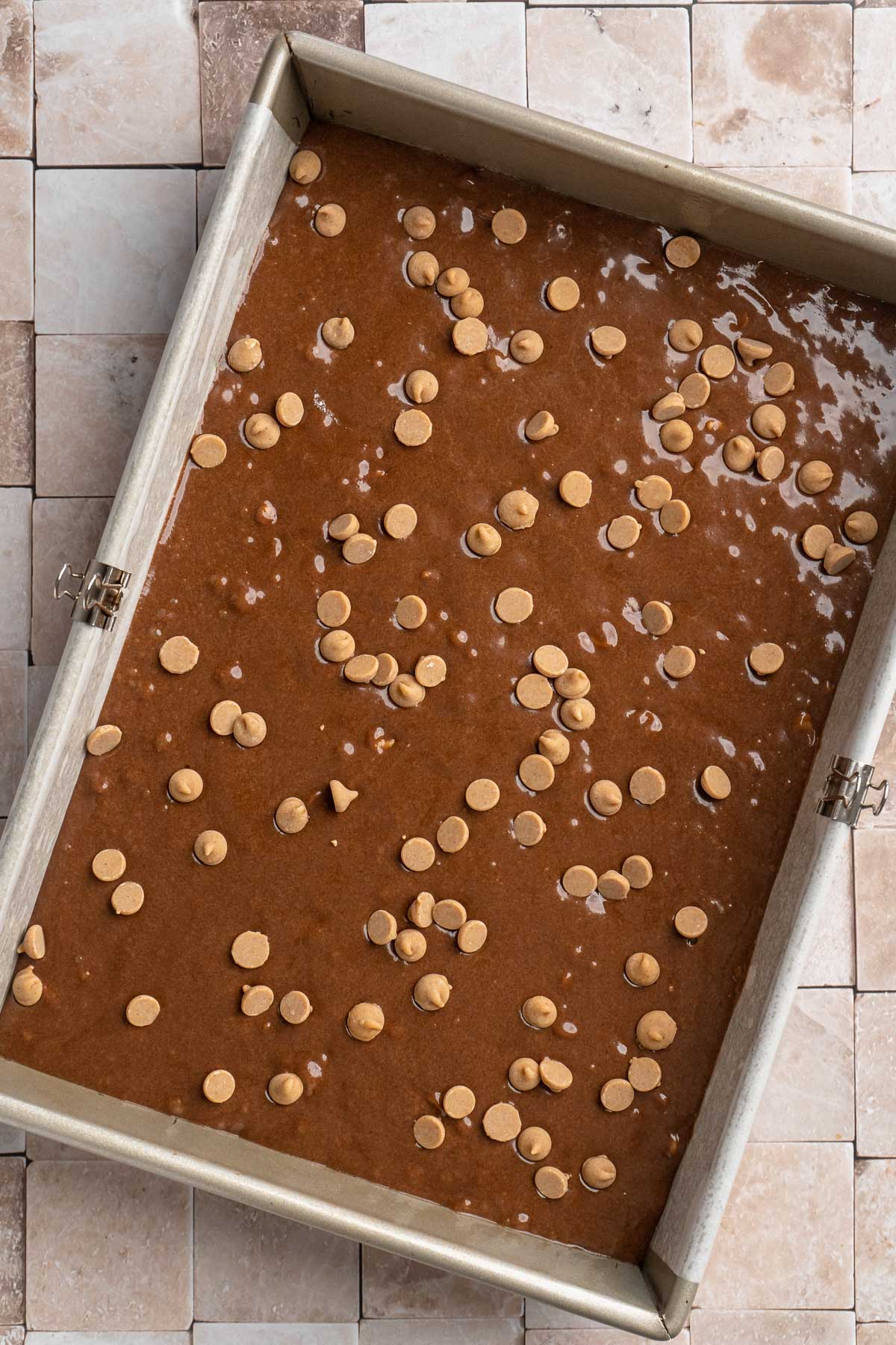 Brownie batter topped with peanut butter chips in a pan.