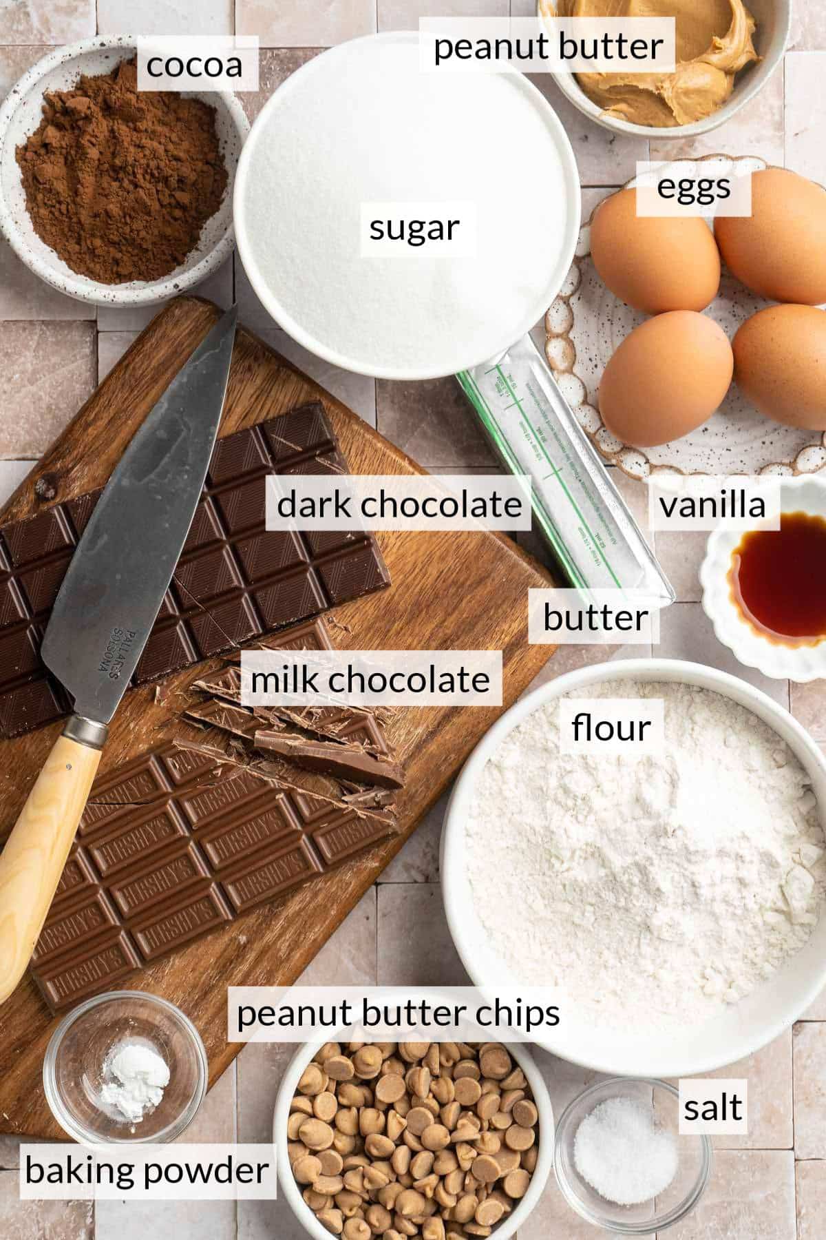 Bowls with flour, cocoa powder peanut butter, sugar and vanilla near a cutting board with chocolate.