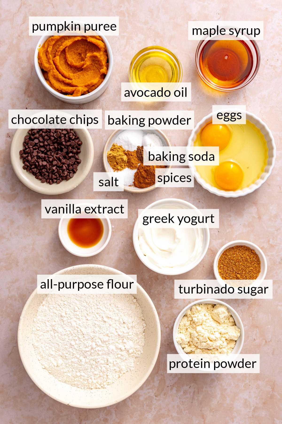 Small bowls with flour, protein powder, eggs, Greek yogurt, pumpkin and spices.