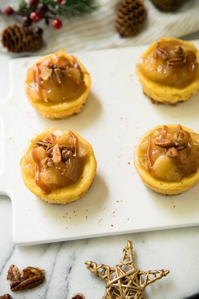Easy Salted Caramel Mini Cheesecakes are the best holiday treat idea! Luscious mini cheesecakes get topped with cinnamon apples and a drizzle of salted caramel to make all of your dessert dreams come true!