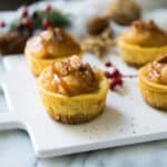 Easy Salted Caramel Mini Cheesecakes are the best holiday treat idea! Luscious mini cheesecakes get topped with cinnamon apples and a drizzle of salted caramel to make all of your dessert dreams come true!