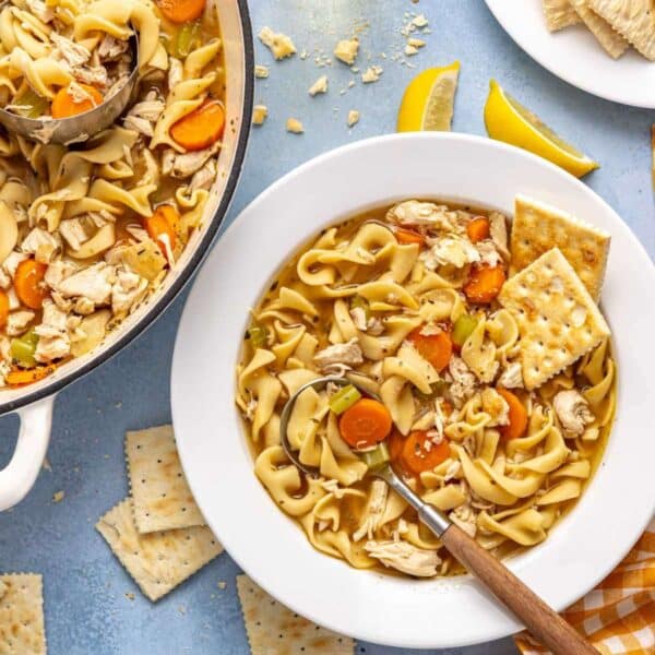Chicken noodle soup served in a white bowl with a spoon and saltine crackers.