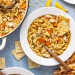 Chicken noodle soup served in a white bowl with a spoon and saltine crackers.