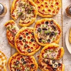 Mini pizzas on a wire rack topped with mini pepperonis and other assorted toppings.