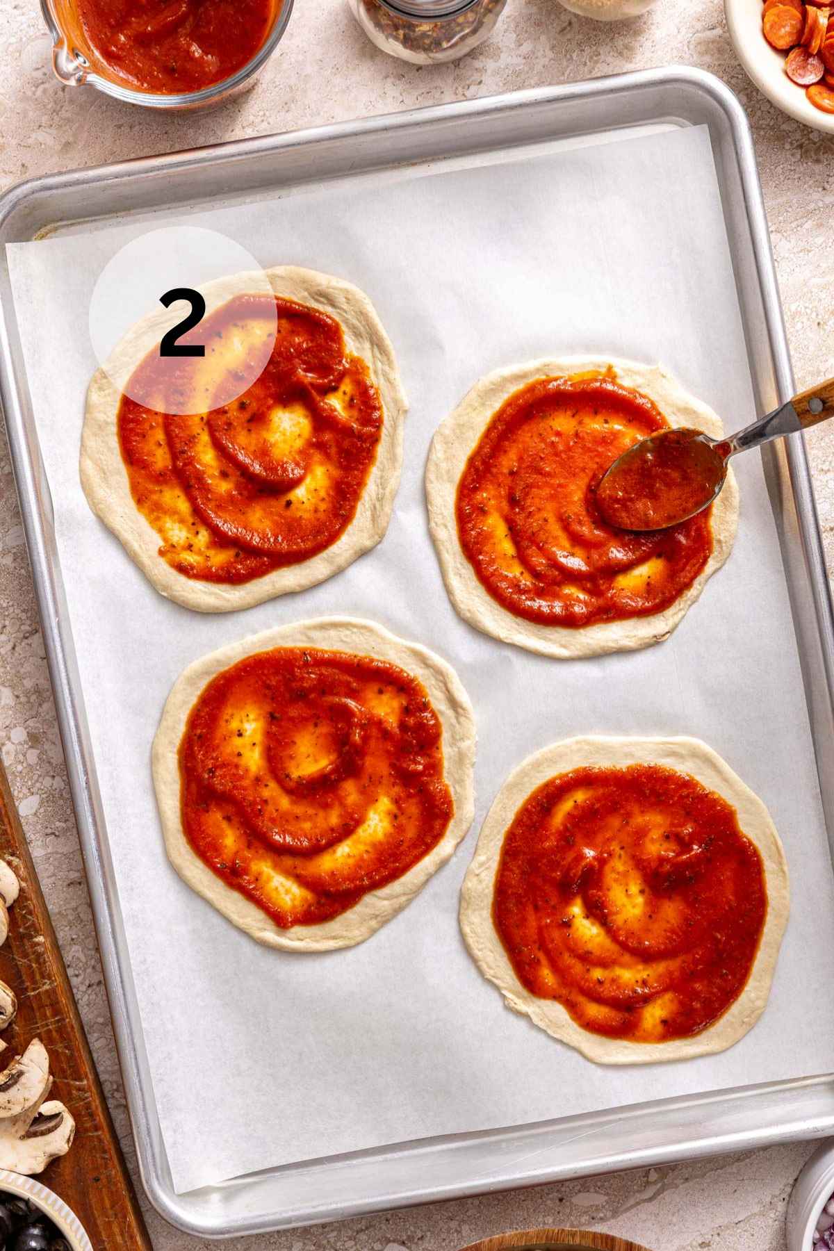 Spreading sauce with a spoon on small rounds of dough.