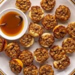 Pecan tartlets on a plate with a small bowl of caramel.