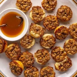 Pecan tartlets on a plate with a small bowl of caramel.