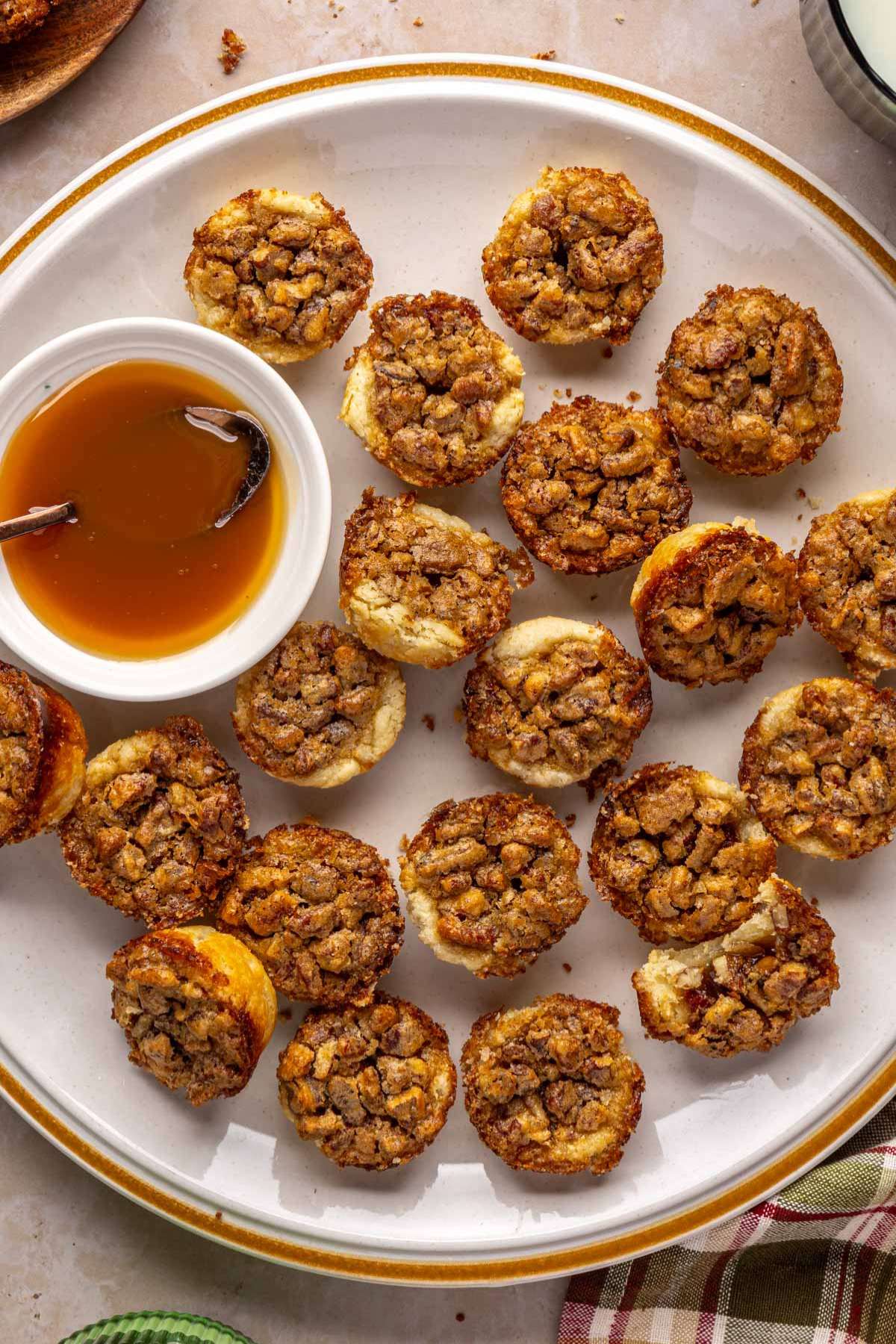 Pecan tartlets on a plate with a small bowl of caramel.