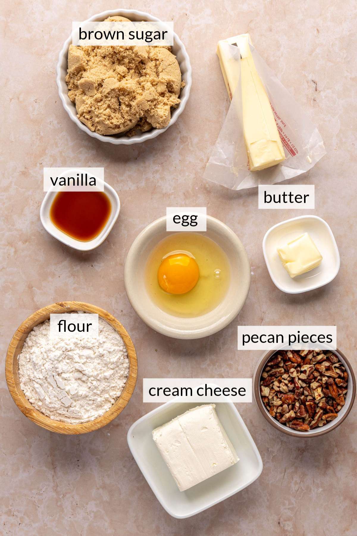Bowls filled with sugar, butter, egg, vanilla, flour, pecan and cream cheese.