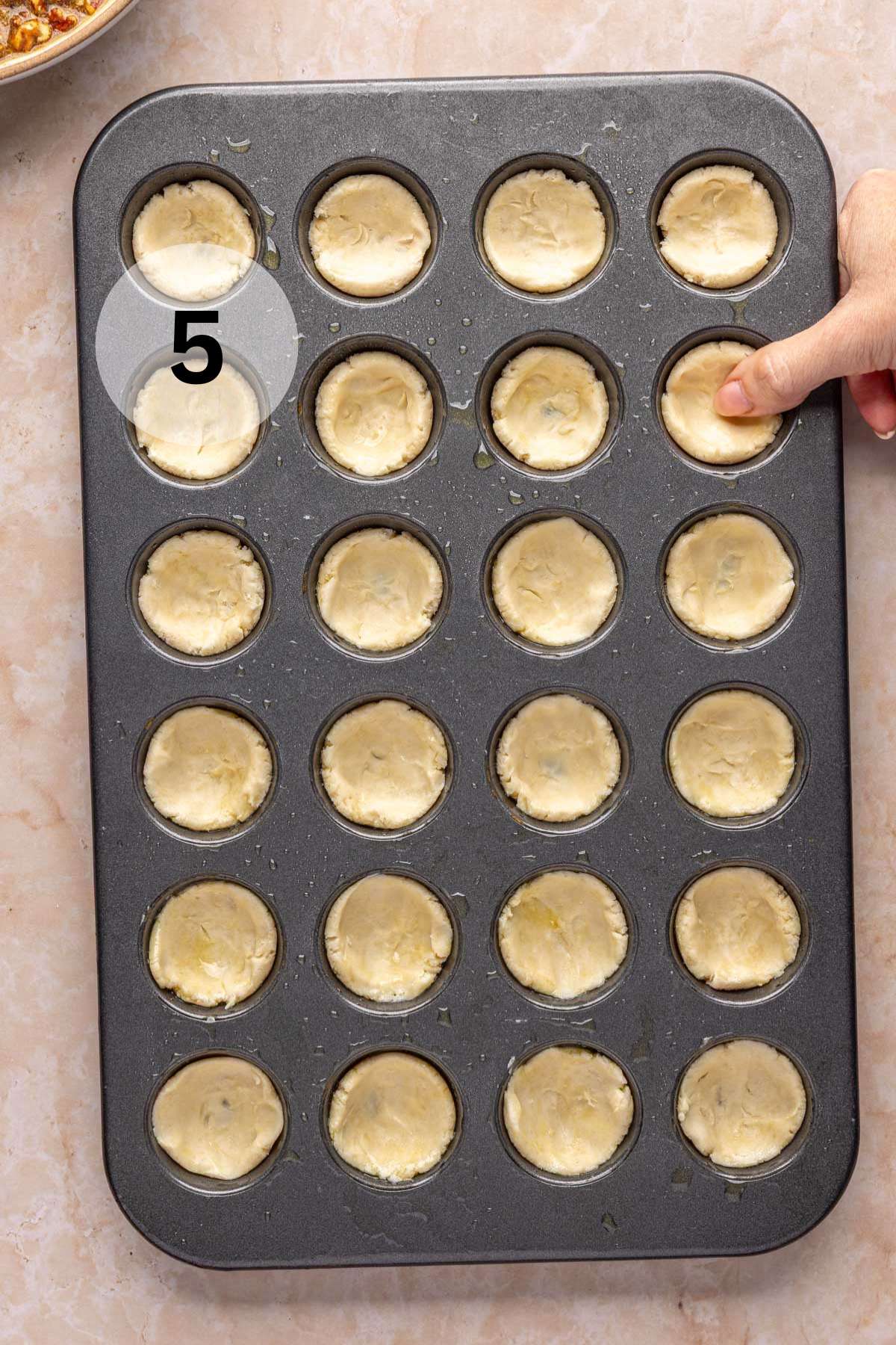 Pressing dough into a mini muffin pan.