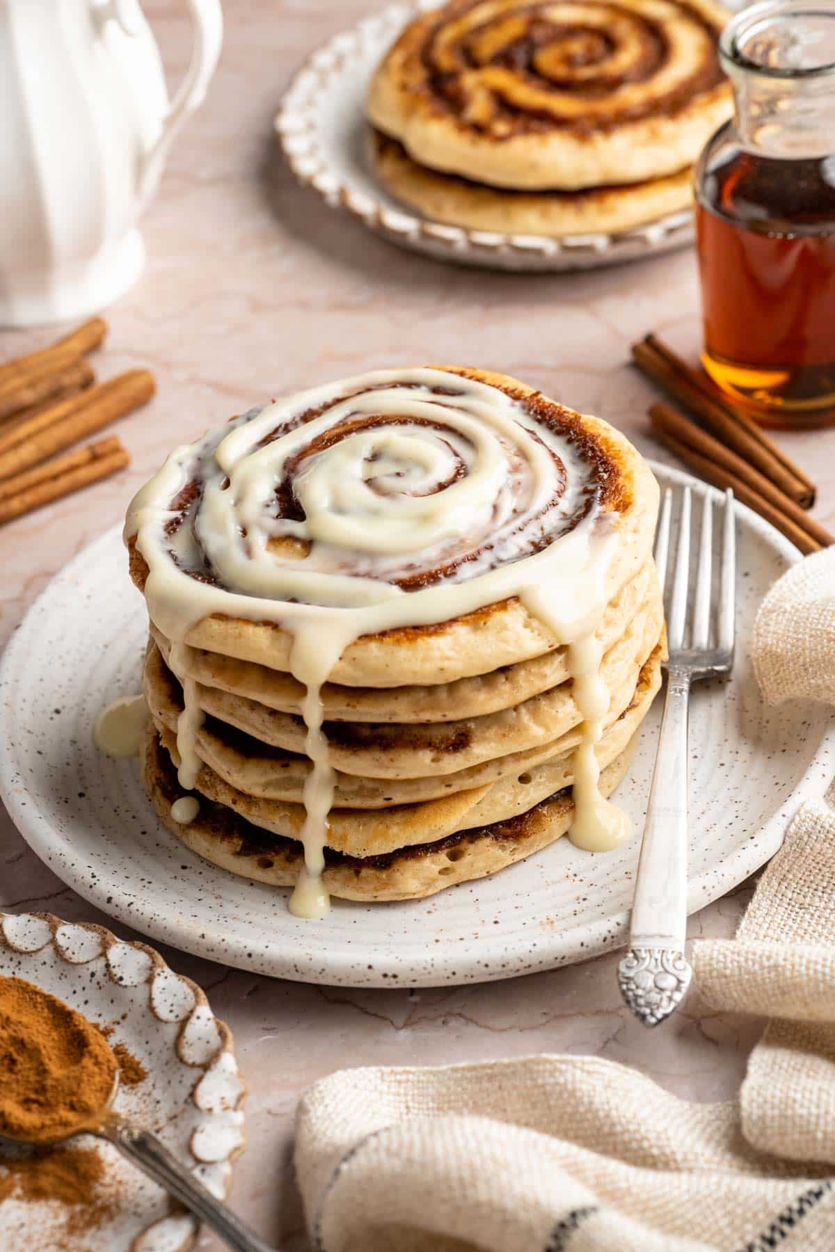 A stack of cinnamon roll pancakes with glaze dripping down the sides.