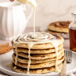 Drizzling glaze over a stack of cinnamon roll pancakes.