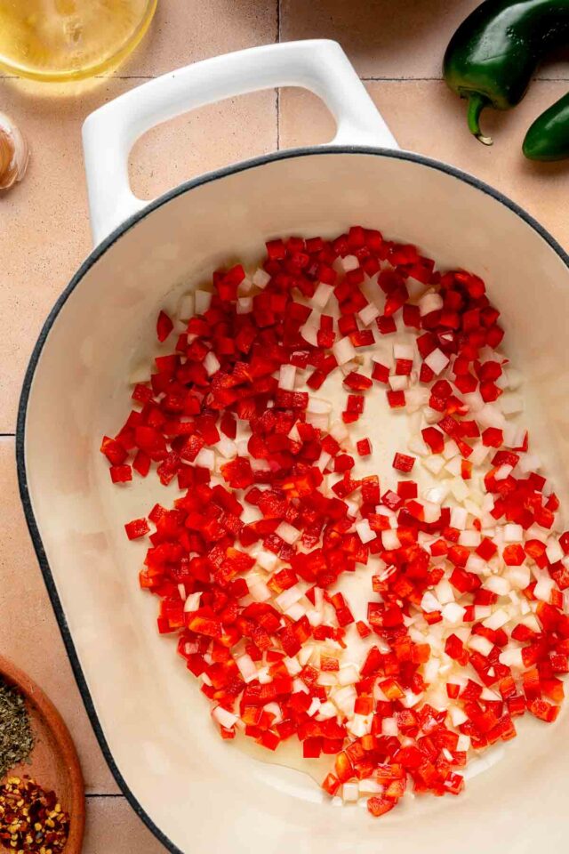 Red bell pepper sautéing with onion in a large pot.