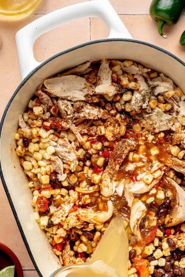Adding shredded chicken, corn, black beans and tomatoes to cooked veggies in a pot.