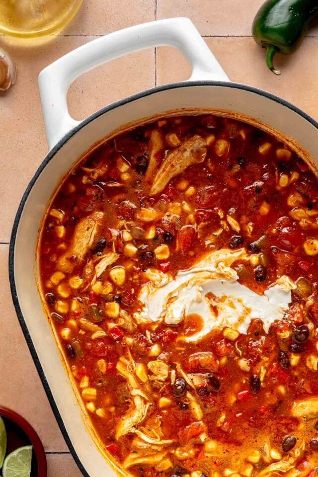 Adding cream cheese to a cooking Mexican soup in a pot.