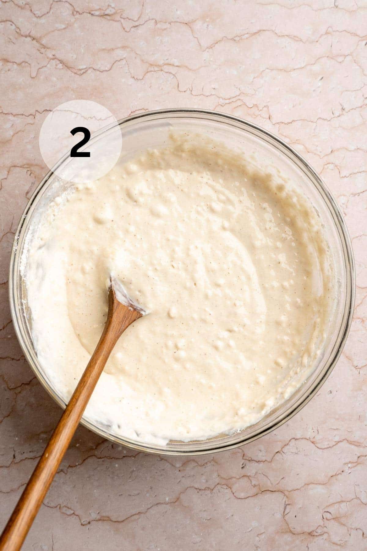 Using a wooden spoon to stir pancake batter in a large bowl.