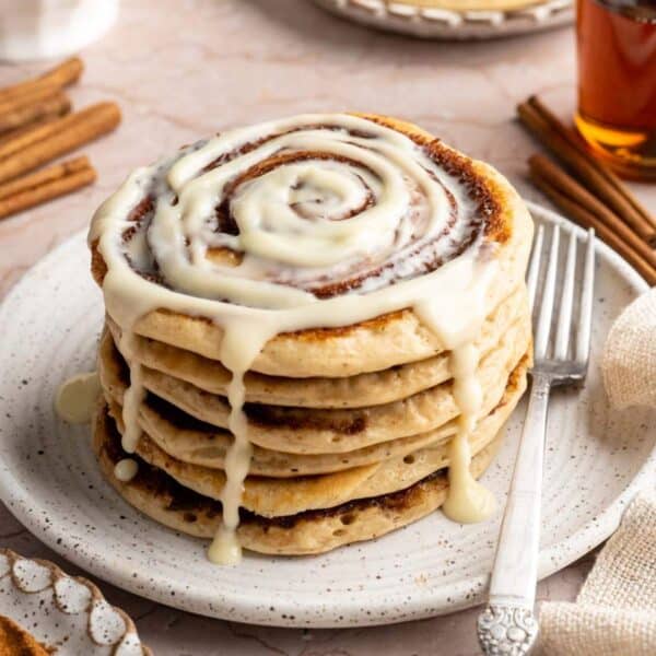 A stack of cinnamon roll pancakes with glaze dripping down the sides.