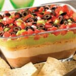 7 layer dip in a glass serving dish with tortilla chips.