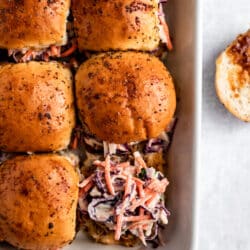 sliders in a casserole dish topped with pork and coleslaw