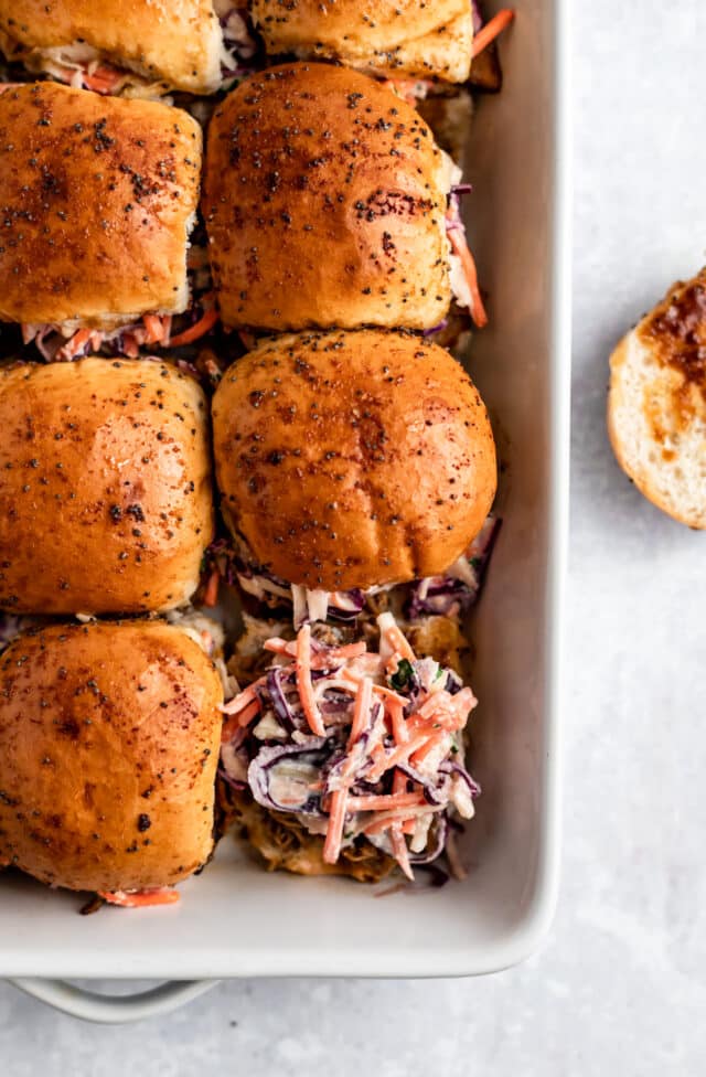 sliders in a casserole dish topped with pork and coleslaw