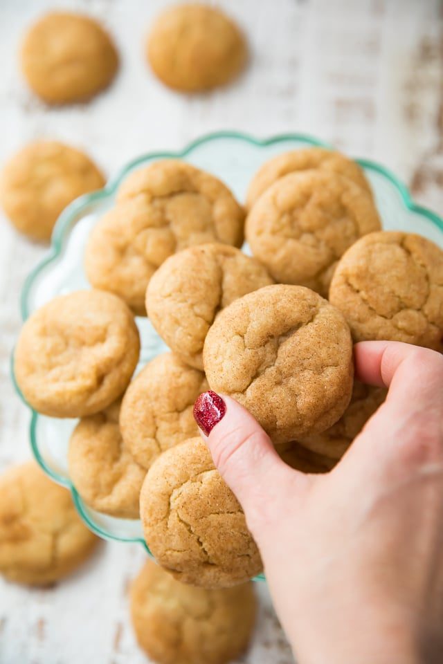 Snickerdoodle Cookies on a glass plate with a woman's hand reaching for one