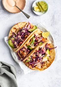 three cod fish tacos topped with slaw, sauce and sliced avocado