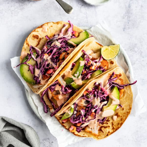 three cod fish tacos topped with slaw, sauce and sliced avocado
