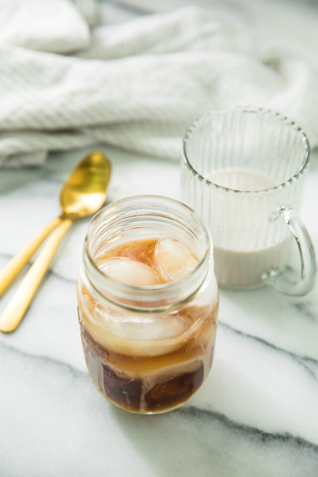cold brew coffee in a mason jar sitting next to a glass of milk and two gold spoons 