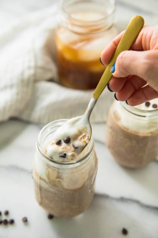 woman's handing holding gold spoon dipping out a bite of Cold Brew Coffee Overnight Protein Oats from a jar