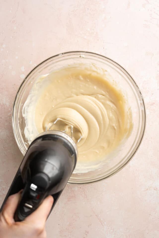 Mixing cream cheese with sugar using an electric mixer.