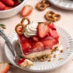 Slice of strawberry pretzel salad on a white plate with a fork.