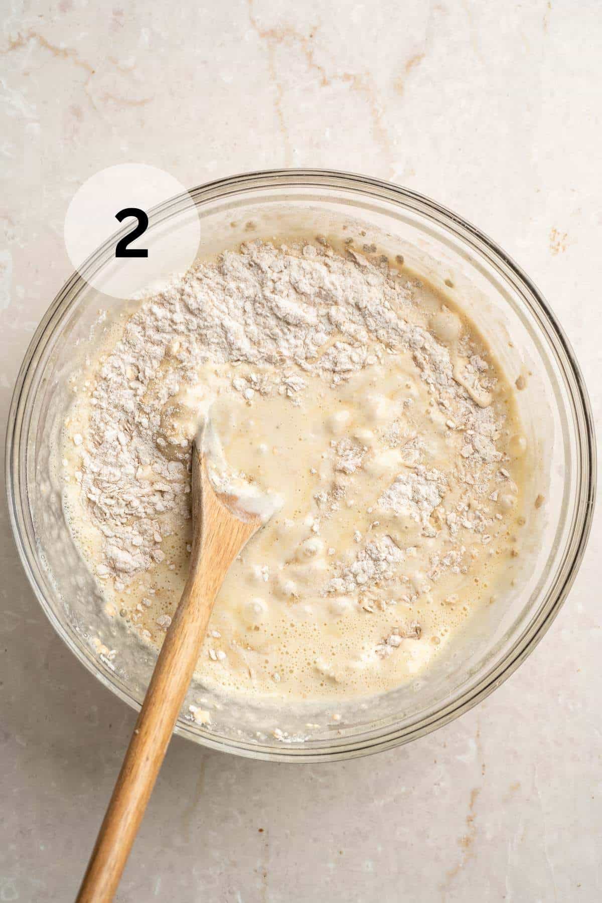 Using a wooden spoon to stir wet ingredients into dry ingredients in a large bowl.