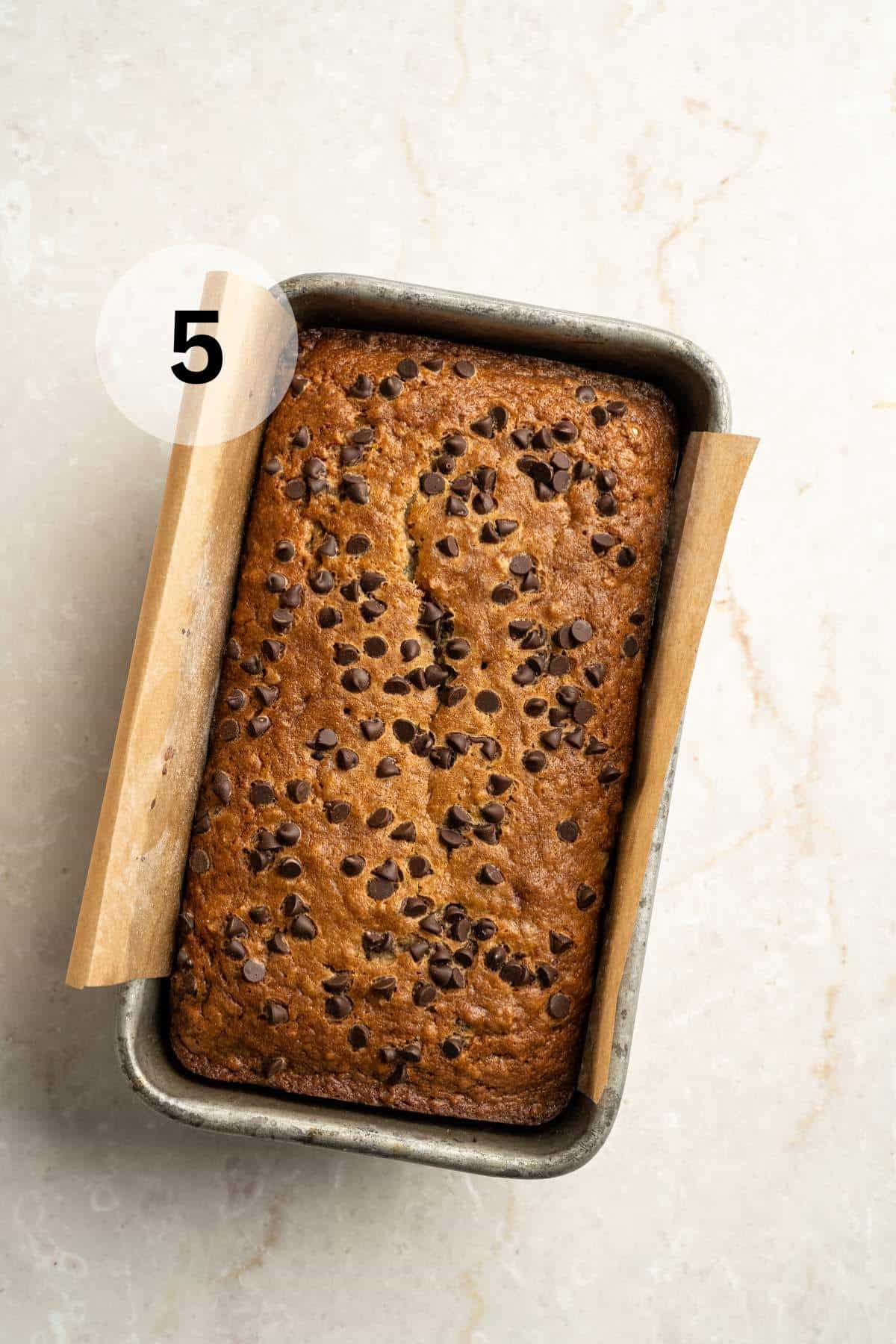 Baked banana bread in a parchment lined loaf pan.