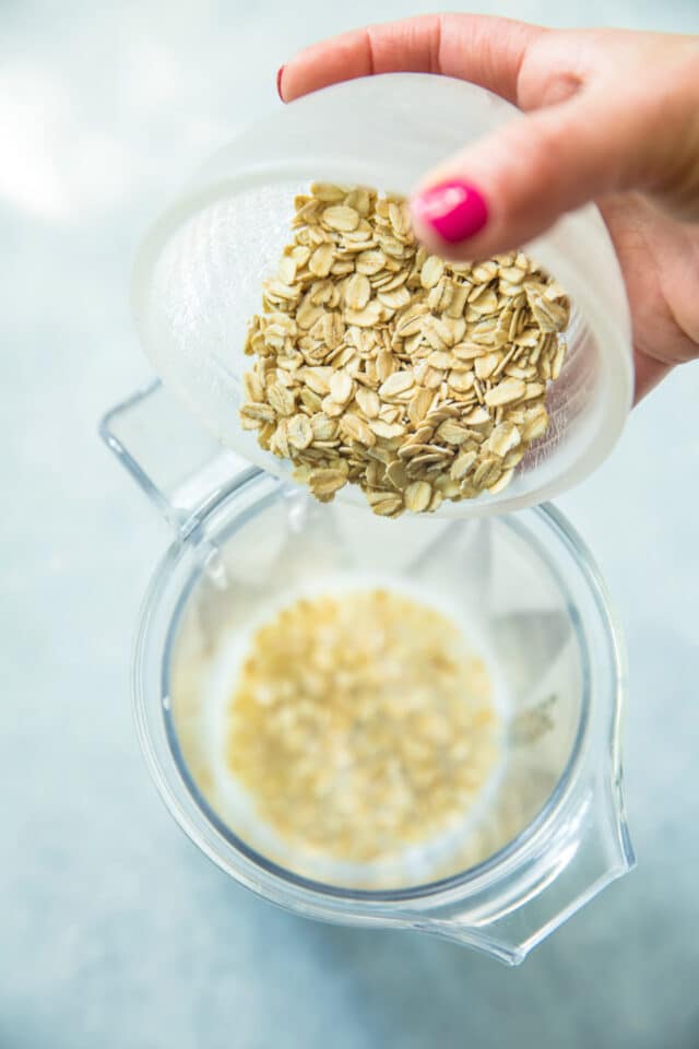 hand pouring oats into blender for healthy protein waffle recipe