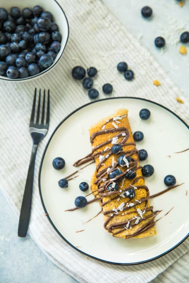 overhead view of Nutella Blueberry Protein Crepes on a white plate with a black fork