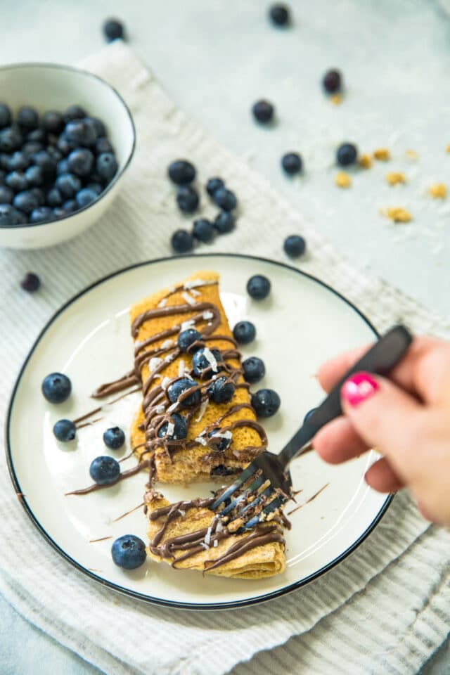 woman's hand using a black fork to take a bite of Nutella Blueberry Protein Crepes 