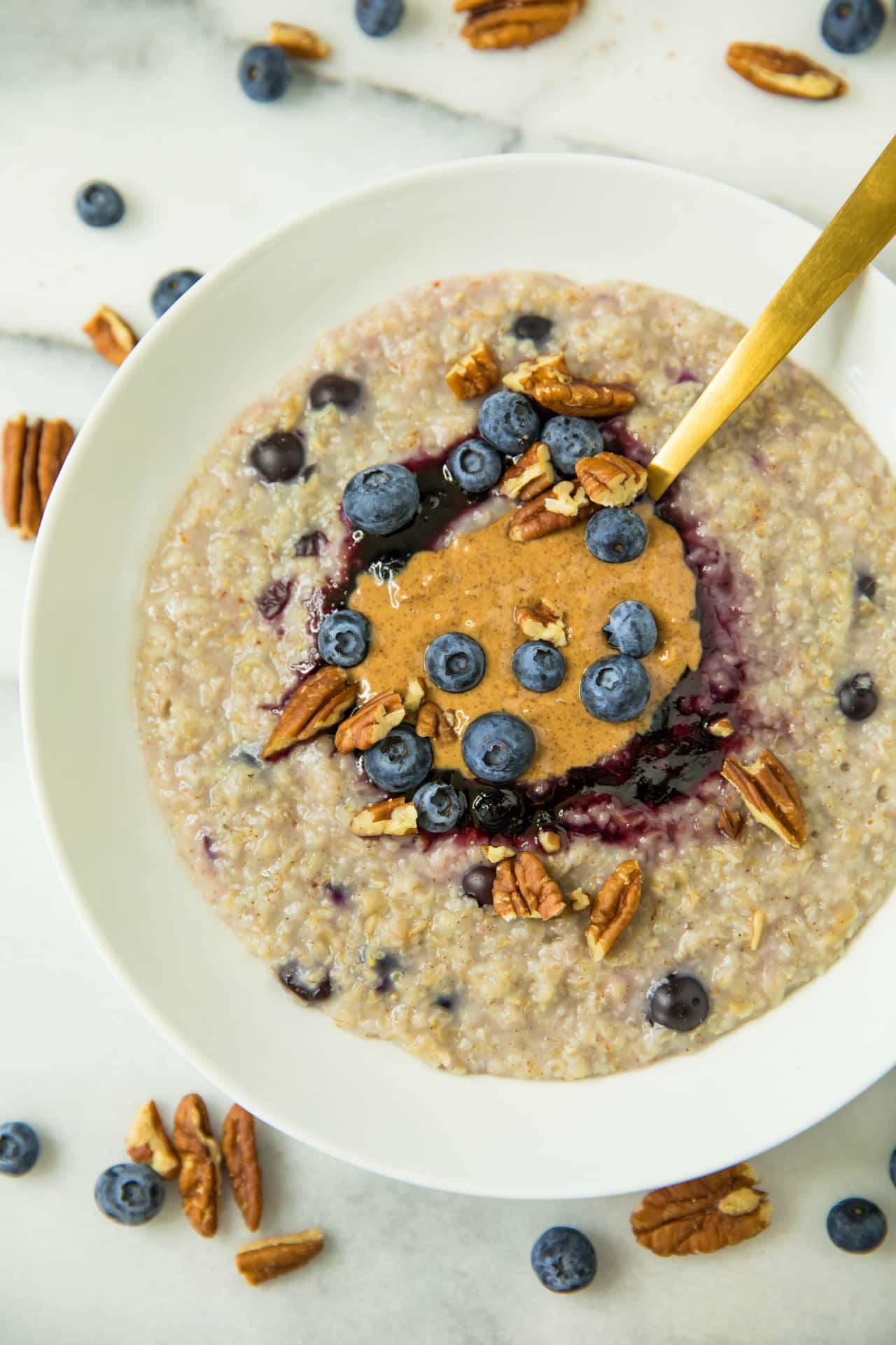 oatmeal in a white bowl topped with blueberries, almond butter, pecans and blueberry jam