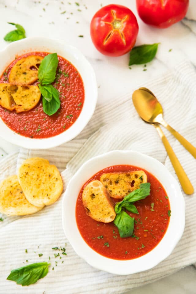 overhead view of Healthy Roasted Tomato Basil Soup in white bowls with gold spoons