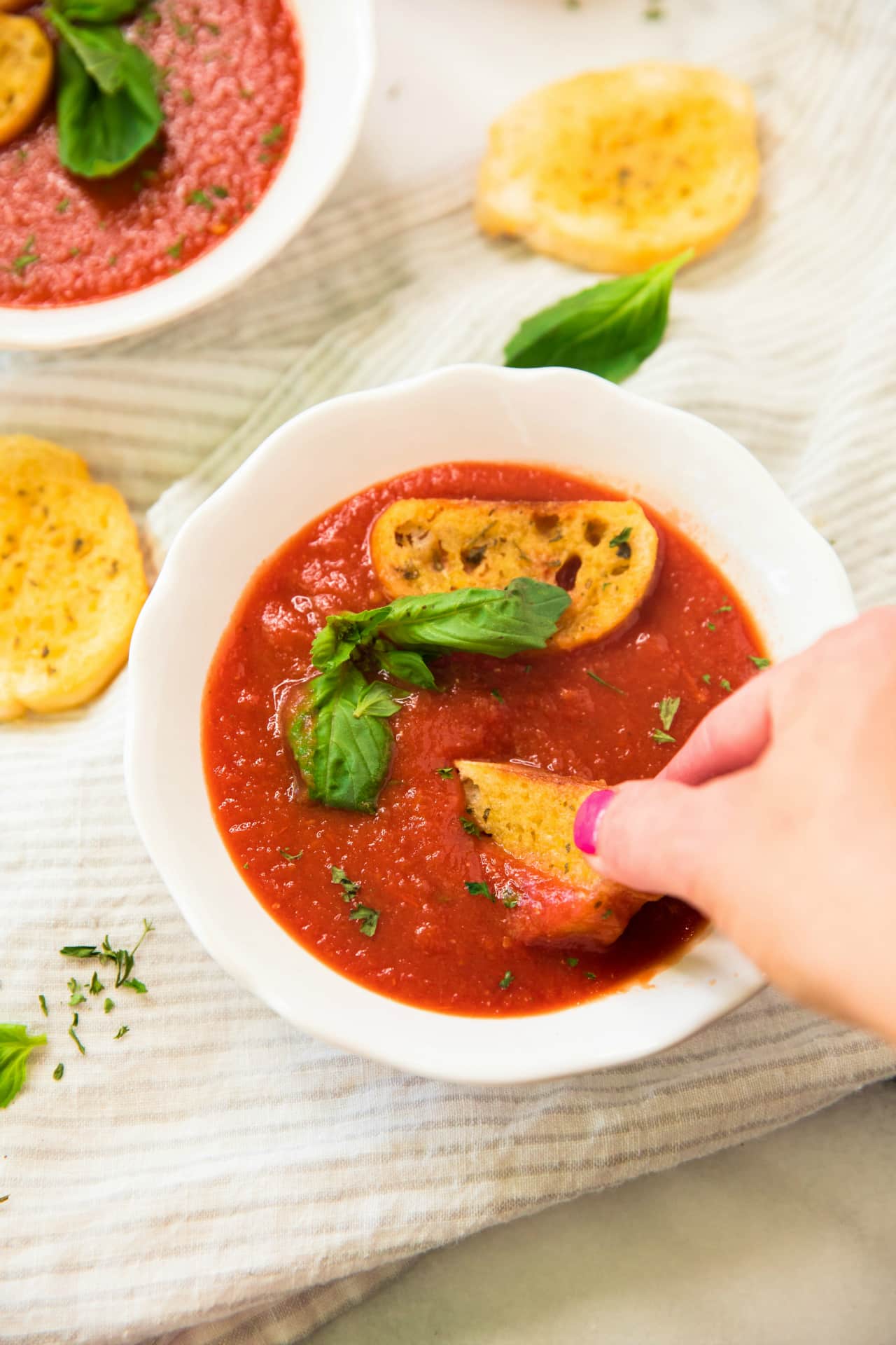 overhead view of woman's hand dipping garlic bread into Healthy Roasted Tomato Basil Soup