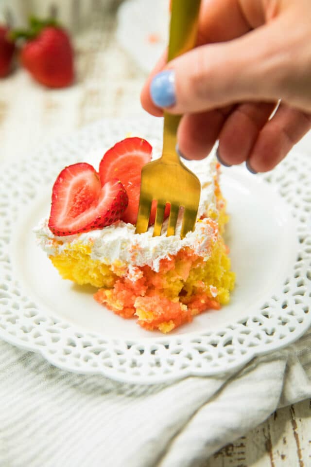 woman's hand using a gold fork to get a bite of an Easy Strawberry Lemonade Poke Cake