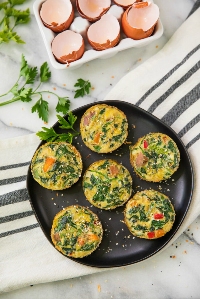 overhead view of Healthy Sweet Potato Spinach Egg Cups on a black plate with cracked eggs in the background