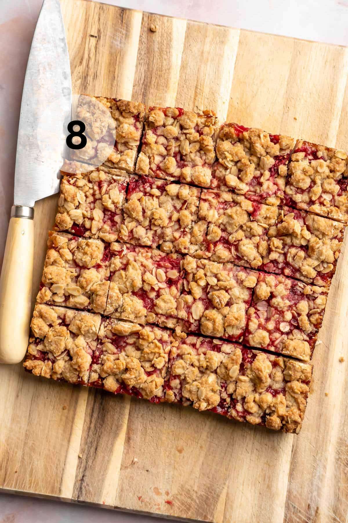 Raspberry bars cut into squares on a cutting board.