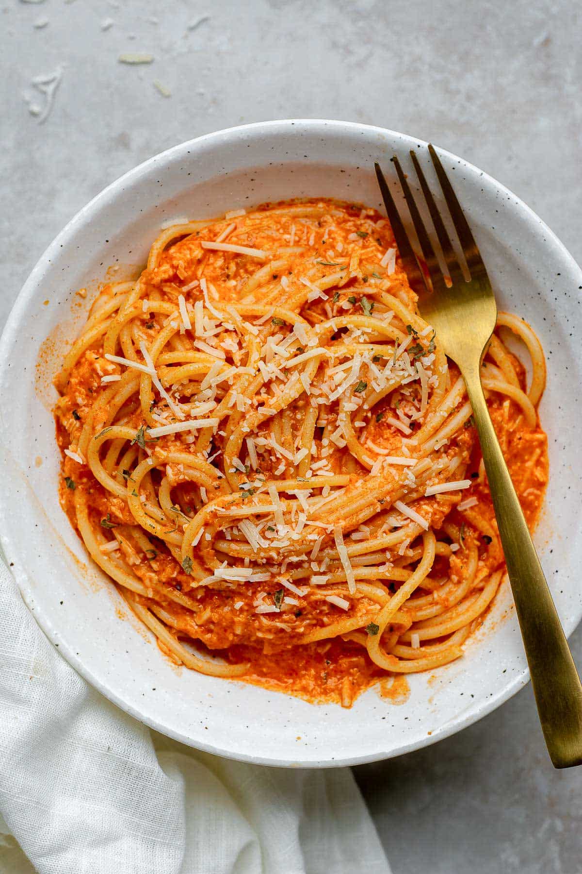 Spaghetti served with roasted red pepper sauce in a white bowl with a fork.
