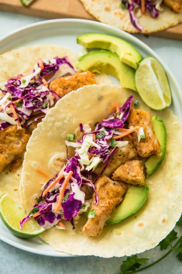 closeup view of Healthy Blackened Baja Fish Tacos served on a white plate with lime slices and avocado slices