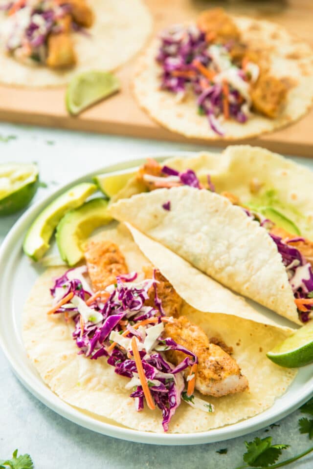 Healthy Blackened Baja Fish Tacos served on a white plate with lime slices and avocado slices