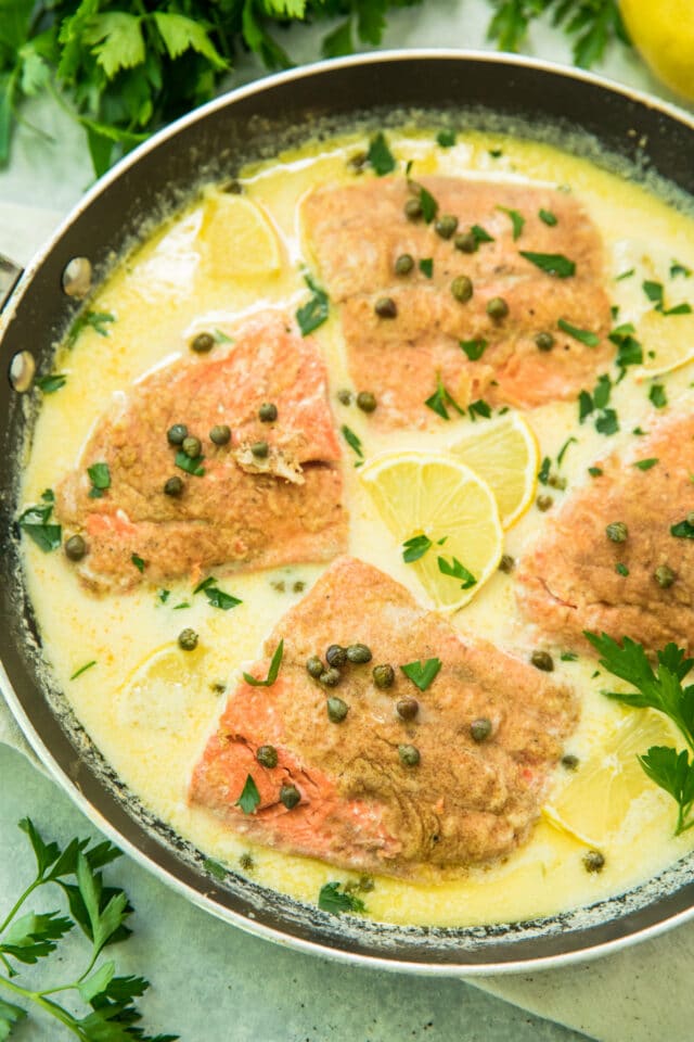 overhead view of Creamy Salmon Piccata in the skillet garnished with parsley and lemon slices