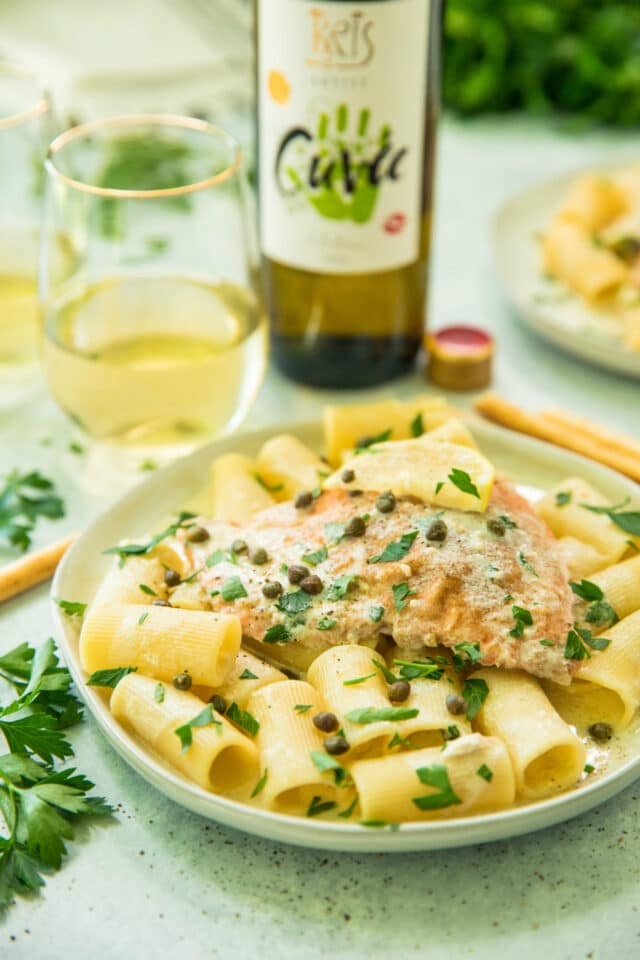 side view of Creamy Salmon Piccata served over pasta with wine and breadsticks